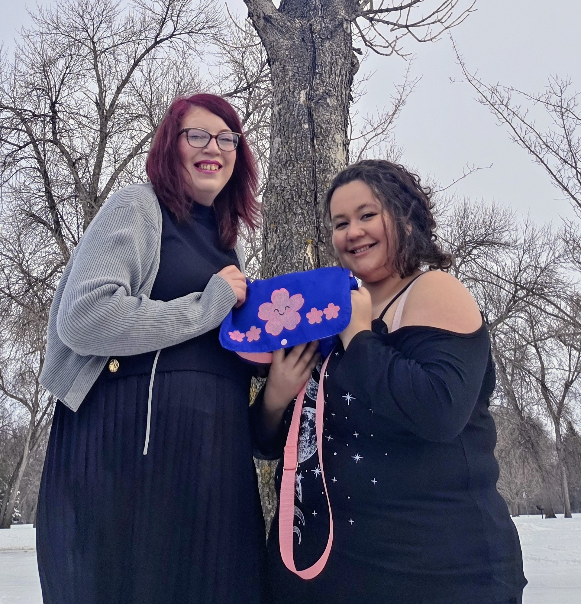 two women in black holding up a royal blue purse with kawaii light pink glitter iron on vinyl cherry blossoms on the flap.