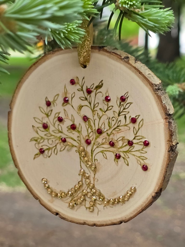 A wooden round ornament with a bejeweled ydrasil (tree of life) on it in gold and burgundy
