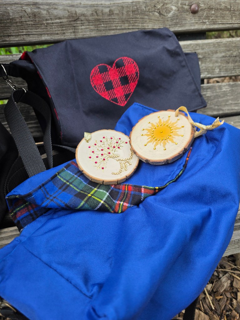 a black diaper purse with a red glitter plaid heart ironed on the flap, sitting behind a blue diaper purse lined in blue and red plaid, with two solstice ornaments sitting on top